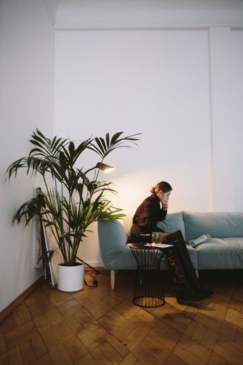 En dame som sitter i en sofa ved siden av en palme plante 